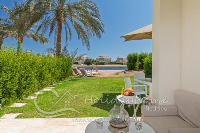 Terrace with cozy sitting pillows, dining table, umbrella and sunbeds in the garden